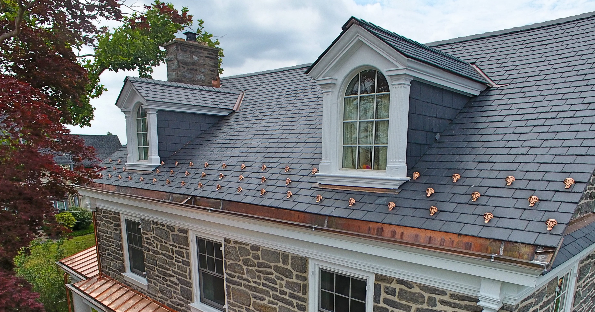 High-performance copper pad-style snow guards retrofitted to natural slate tile roof on historic home.